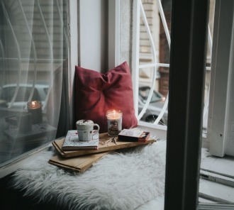 cozy corner with pillow, blanket, candle, hot drink, and a book