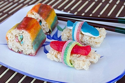 Four sushi rolls made from rice krispy treats and candy sit on a white plate