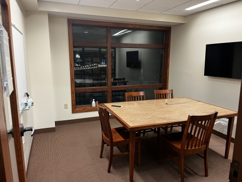 A room with a table and 4 chairs, a white board, and a TV monitor