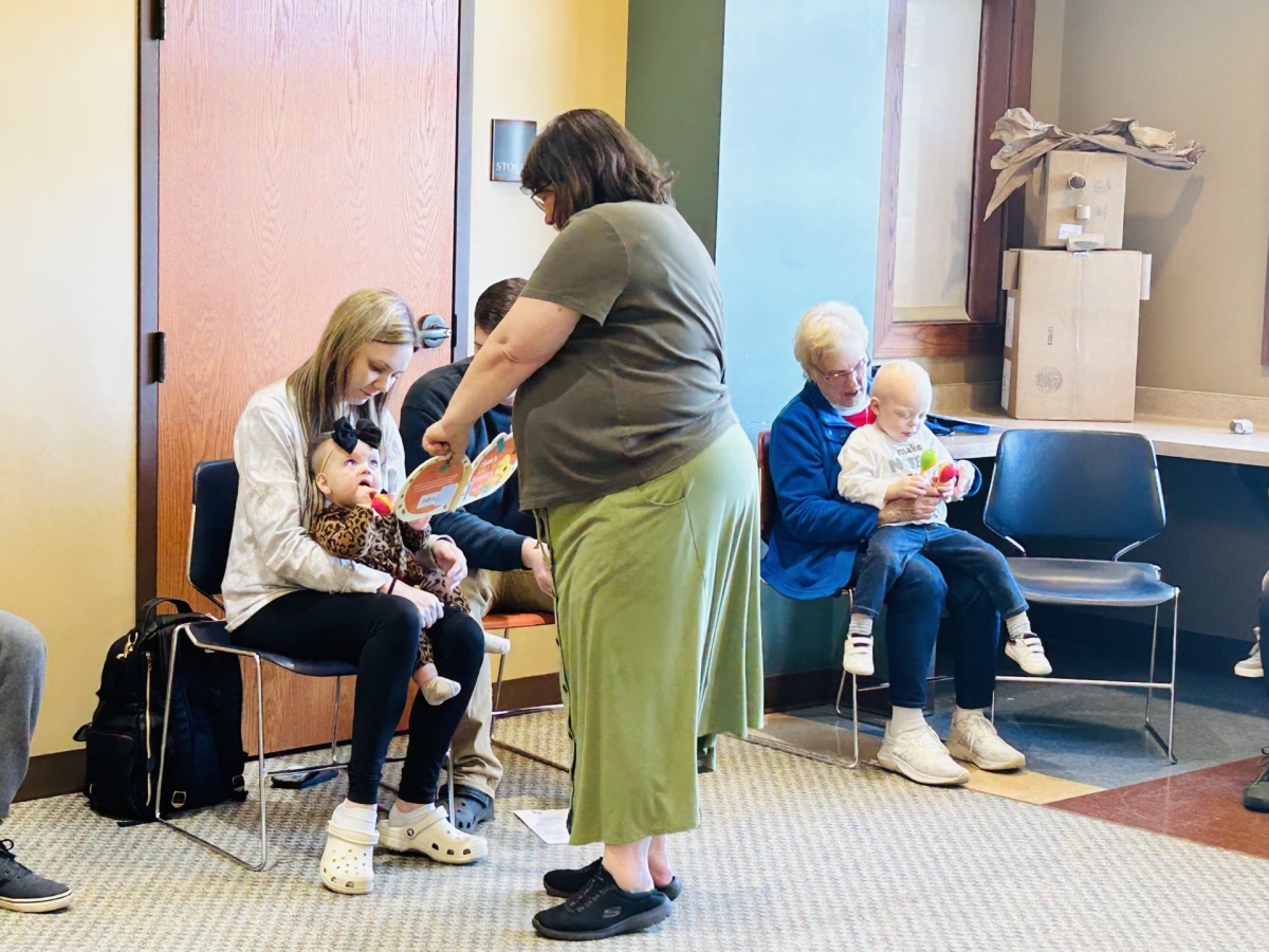 Baby sitting in adult's lap while librarian shows them a book