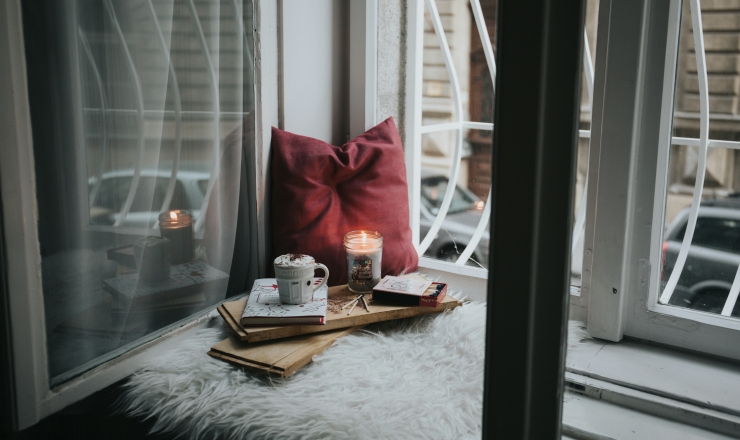 cozy corner with pillow, blanket, candle, hot drink, and a book